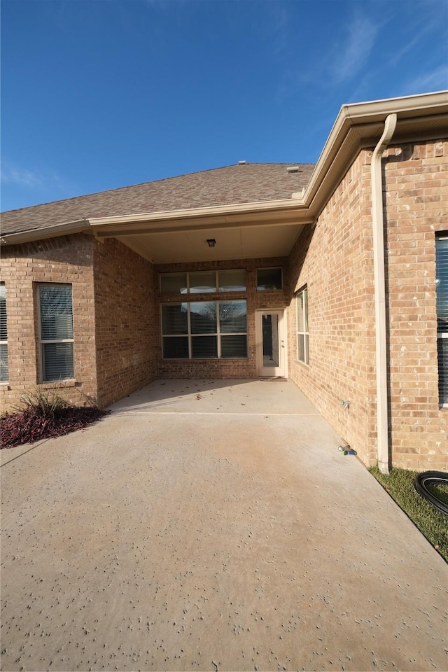 doorway to property featuring brick siding and a shingled roof