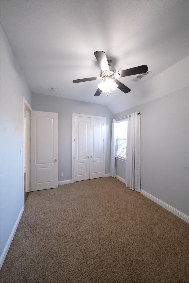 unfurnished bedroom featuring baseboards, visible vents, vaulted ceiling, a closet, and light carpet