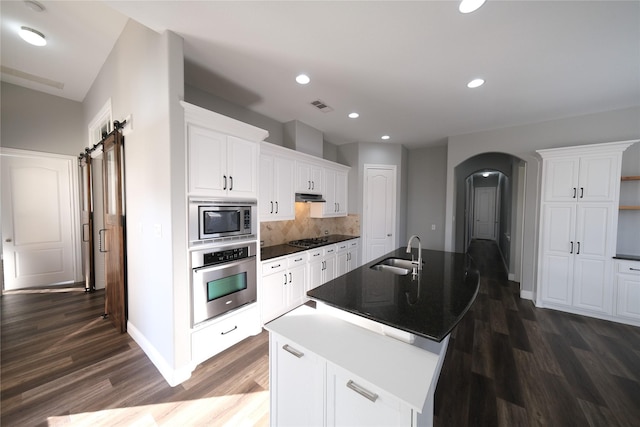 kitchen featuring tasteful backsplash, a barn door, appliances with stainless steel finishes, arched walkways, and a sink