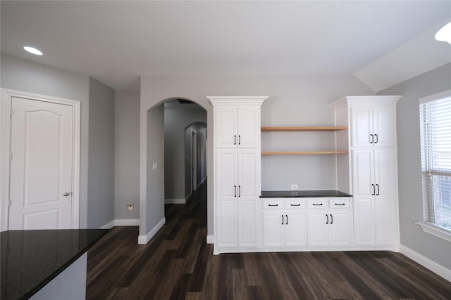 kitchen with dark wood-type flooring, open shelves, white cabinetry, arched walkways, and baseboards