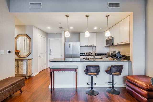 kitchen featuring sink, stainless steel appliances, pendant lighting, wood-type flooring, and white cabinets