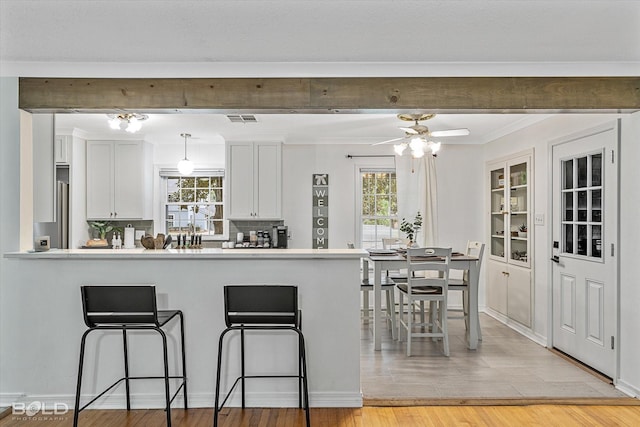 kitchen with pendant lighting, backsplash, ceiling fan, light wood-type flooring, and white cabinetry