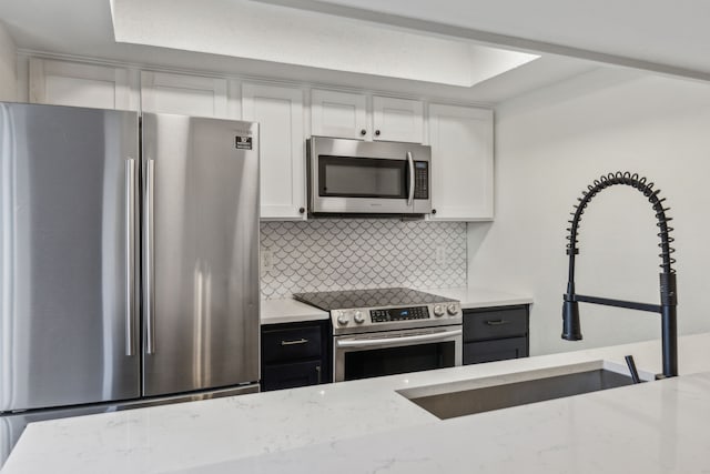 kitchen featuring white cabinets, decorative backsplash, light stone counters, and appliances with stainless steel finishes