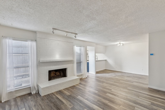 unfurnished living room featuring a textured ceiling, a healthy amount of sunlight, a fireplace, and track lighting