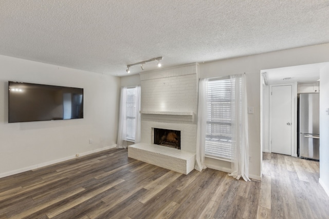 unfurnished living room featuring a textured ceiling, a healthy amount of sunlight, wood-type flooring, and a fireplace