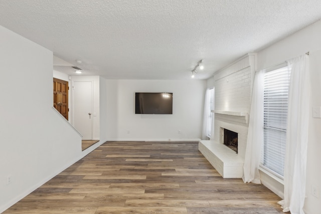 unfurnished living room with a textured ceiling, hardwood / wood-style flooring, a brick fireplace, and rail lighting