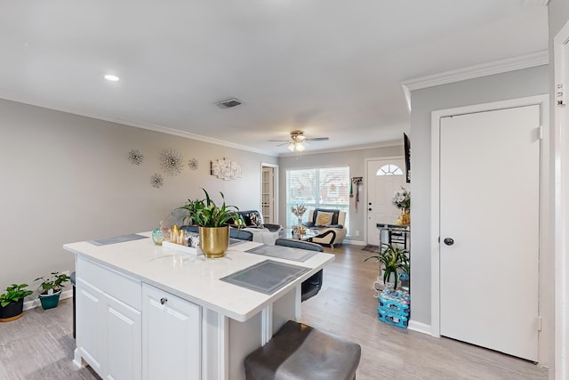 kitchen with white cabinetry, ornamental molding, a center island, ceiling fan, and light wood-type flooring