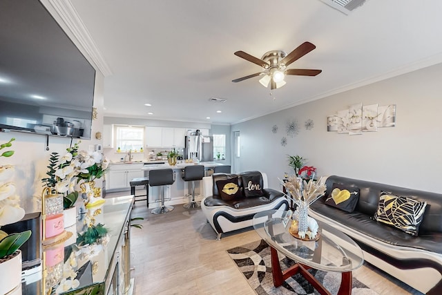 living room featuring ceiling fan, ornamental molding, and light hardwood / wood-style flooring