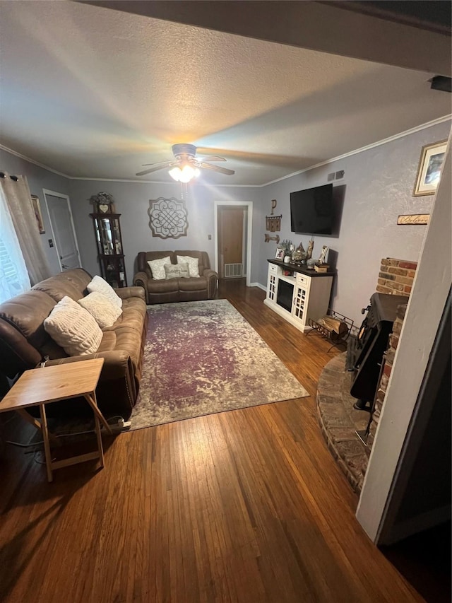 living room featuring ceiling fan, dark wood-type flooring, a textured ceiling, and ornamental molding