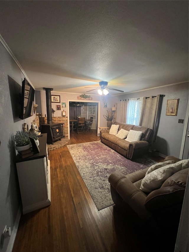 living room featuring ceiling fan, a wood stove, hardwood / wood-style flooring, and ornamental molding