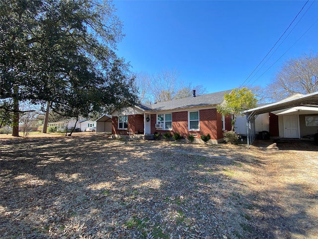 ranch-style home featuring an outbuilding, brick siding, a storage unit, a carport, and driveway