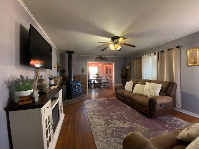 living area with dark wood-type flooring, a wood stove, ornamental molding, and a ceiling fan