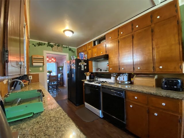 kitchen featuring light stone counters, brown cabinetry, a sink, under cabinet range hood, and black appliances