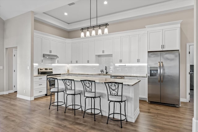 kitchen with a kitchen bar, white cabinetry, under cabinet range hood, appliances with stainless steel finishes, and a kitchen island