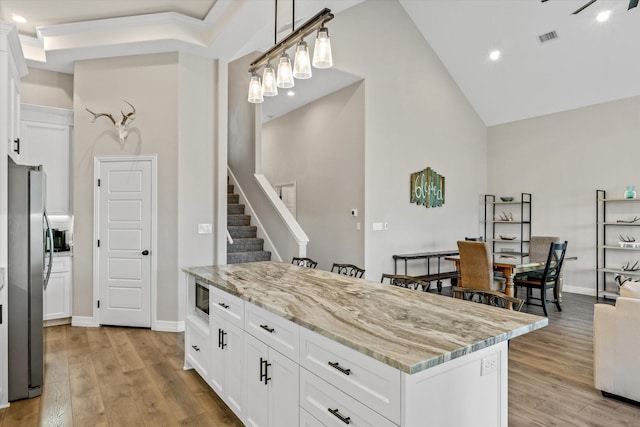 kitchen with pendant lighting, white cabinets, stainless steel appliances, light stone countertops, and light hardwood / wood-style flooring