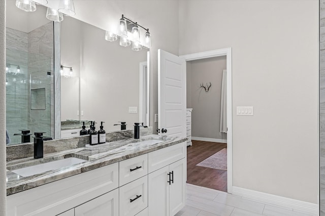 full bath with baseboards, tiled shower, double vanity, and a sink