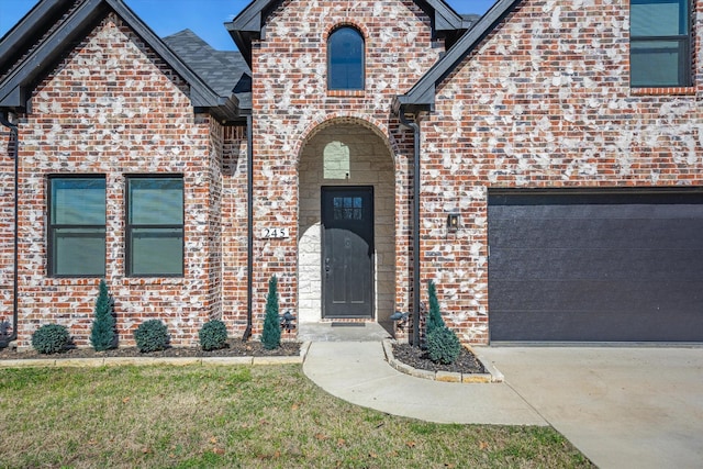 doorway to property featuring brick siding, driveway, and a garage