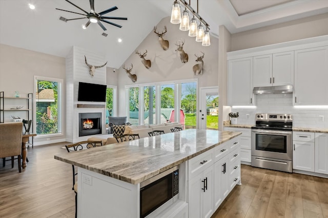kitchen featuring a breakfast bar, high vaulted ceiling, under cabinet range hood, open floor plan, and appliances with stainless steel finishes