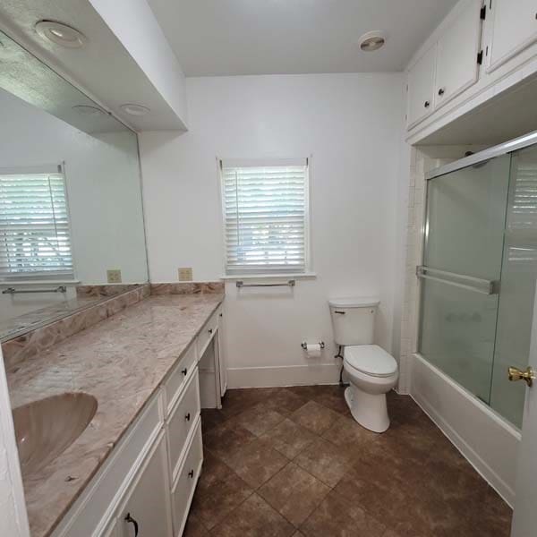 full bathroom with vanity, bath / shower combo with glass door, and toilet