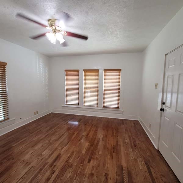 empty room with ceiling fan, dark wood-type flooring, and a textured ceiling