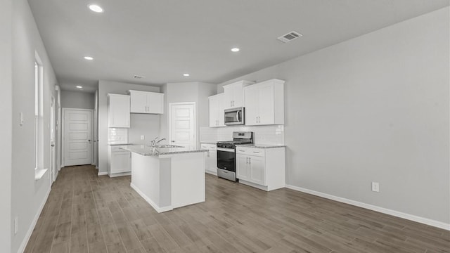 kitchen with a center island with sink, white cabinets, appliances with stainless steel finishes, tasteful backsplash, and light stone counters