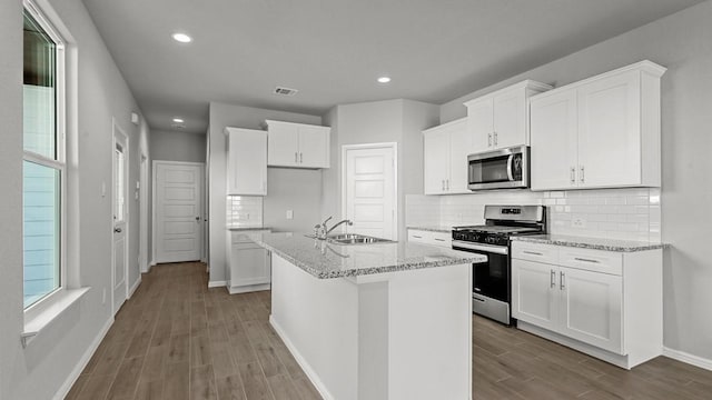 kitchen featuring a center island with sink, white cabinets, sink, light stone countertops, and appliances with stainless steel finishes