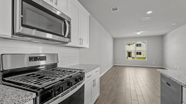 kitchen featuring light stone countertops, tasteful backsplash, wood-type flooring, white cabinets, and appliances with stainless steel finishes