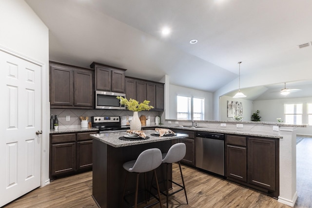 kitchen with tasteful backsplash, a breakfast bar, stainless steel appliances, vaulted ceiling, and a kitchen island