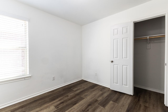 unfurnished bedroom with multiple windows, a closet, and dark wood-type flooring