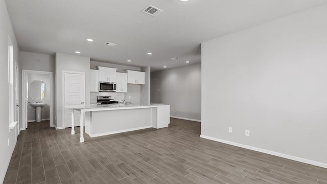 kitchen with dark wood-type flooring, a breakfast bar area, white cabinetry, stainless steel appliances, and a center island with sink