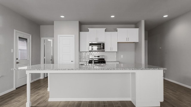 kitchen with white cabinetry, light stone countertops, stainless steel appliances, and a center island with sink