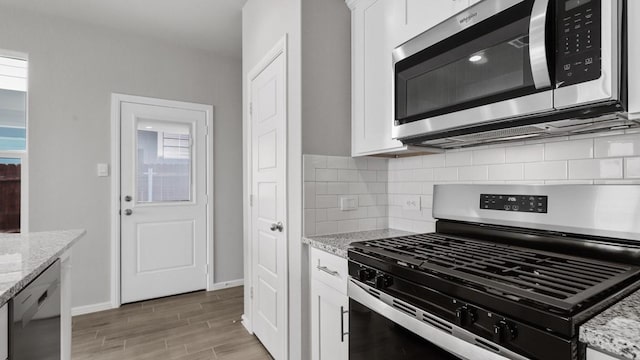 kitchen with white cabinets, stainless steel appliances, light stone counters, and plenty of natural light