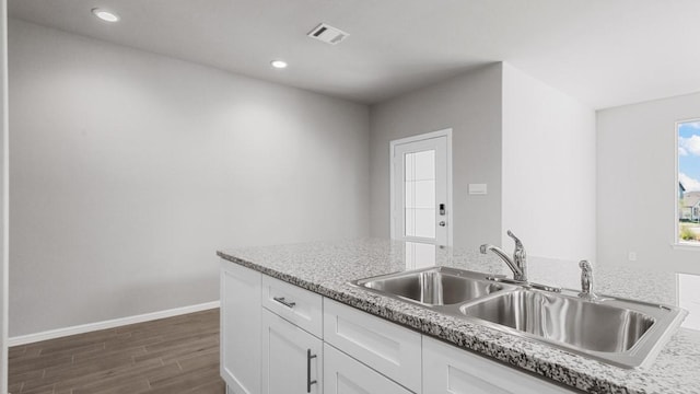 kitchen with dark wood-type flooring, light stone countertops, sink, and white cabinets