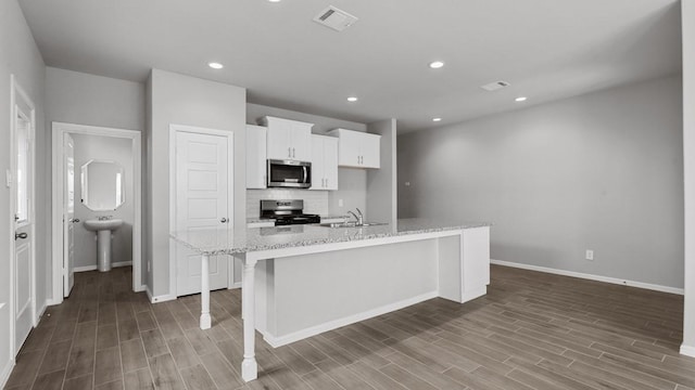 kitchen featuring a breakfast bar, a kitchen island with sink, white cabinets, light stone counters, and stainless steel appliances