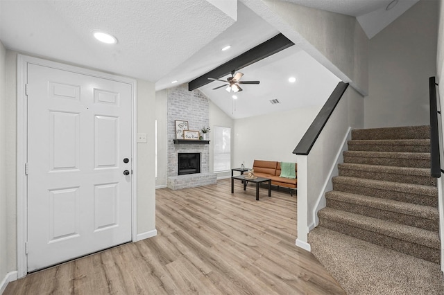 interior space with ceiling fan, lofted ceiling with beams, a textured ceiling, a fireplace, and light wood-type flooring