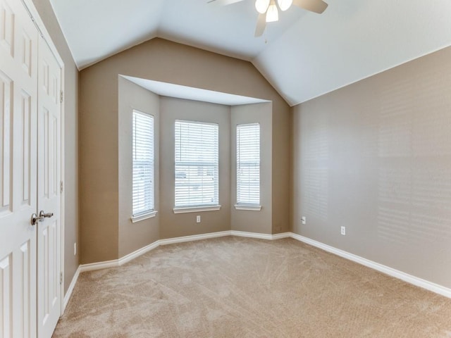 empty room featuring vaulted ceiling, light colored carpet, and ceiling fan