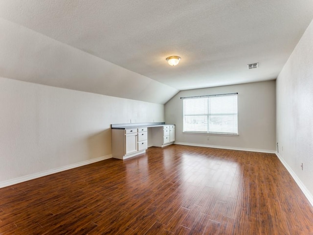 bonus room with built in desk, vaulted ceiling, and dark hardwood / wood-style floors