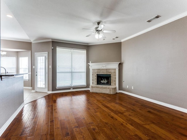 unfurnished living room with ceiling fan with notable chandelier, a brick fireplace, hardwood / wood-style floors, and crown molding