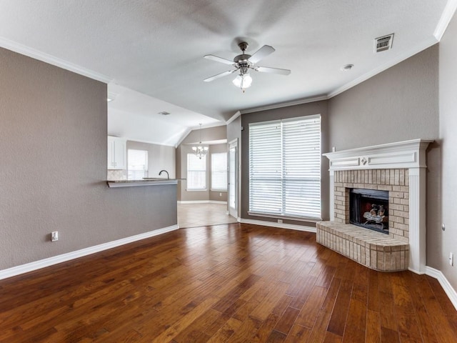 unfurnished living room with ceiling fan with notable chandelier, a fireplace, wood-type flooring, lofted ceiling, and crown molding