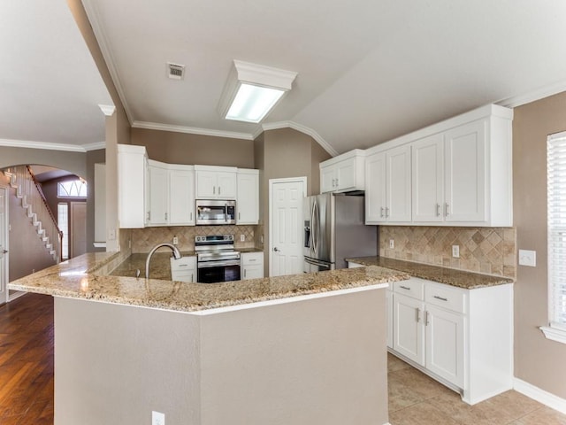 kitchen with light stone counters, appliances with stainless steel finishes, kitchen peninsula, and white cabinets