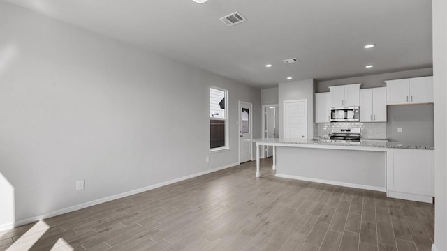 kitchen featuring appliances with stainless steel finishes, white cabinets, decorative backsplash, light stone counters, and light wood-type flooring