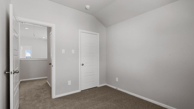 unfurnished bedroom with vaulted ceiling and dark colored carpet