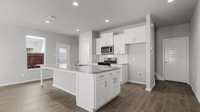 kitchen featuring a kitchen island with sink, light stone countertops, white cabinetry, and stainless steel appliances