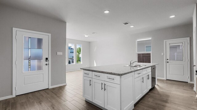 kitchen featuring light stone counters, a kitchen island with sink, sink, dishwasher, and white cabinets