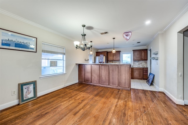 kitchen featuring decorative backsplash, stainless steel refrigerator, hanging light fixtures, and crown molding