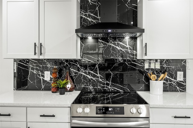 kitchen featuring wall chimney range hood, electric range, light stone countertops, and white cabinets