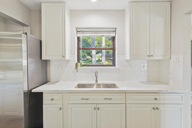 kitchen featuring sink, stainless steel fridge, white cabinetry, and backsplash