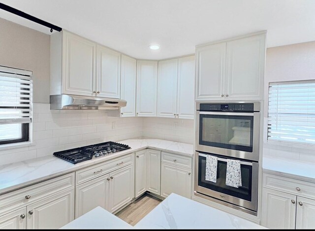 kitchen with backsplash, stainless steel appliances, white cabinets, and light hardwood / wood-style flooring