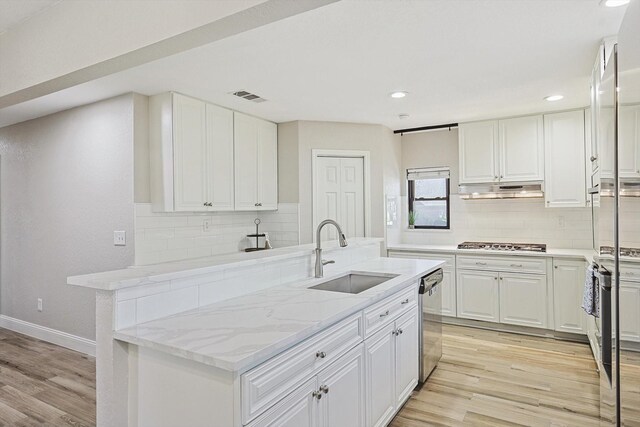 kitchen with white cabinets, light hardwood / wood-style floors, appliances with stainless steel finishes, light stone countertops, and sink