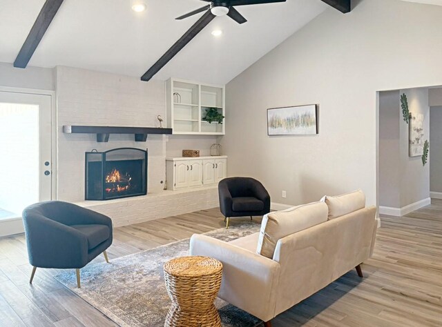 living room with ceiling fan, light hardwood / wood-style flooring, vaulted ceiling with beams, and a fireplace